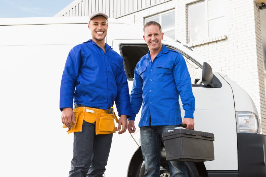 smiling handymen looking at camera in front of their van
